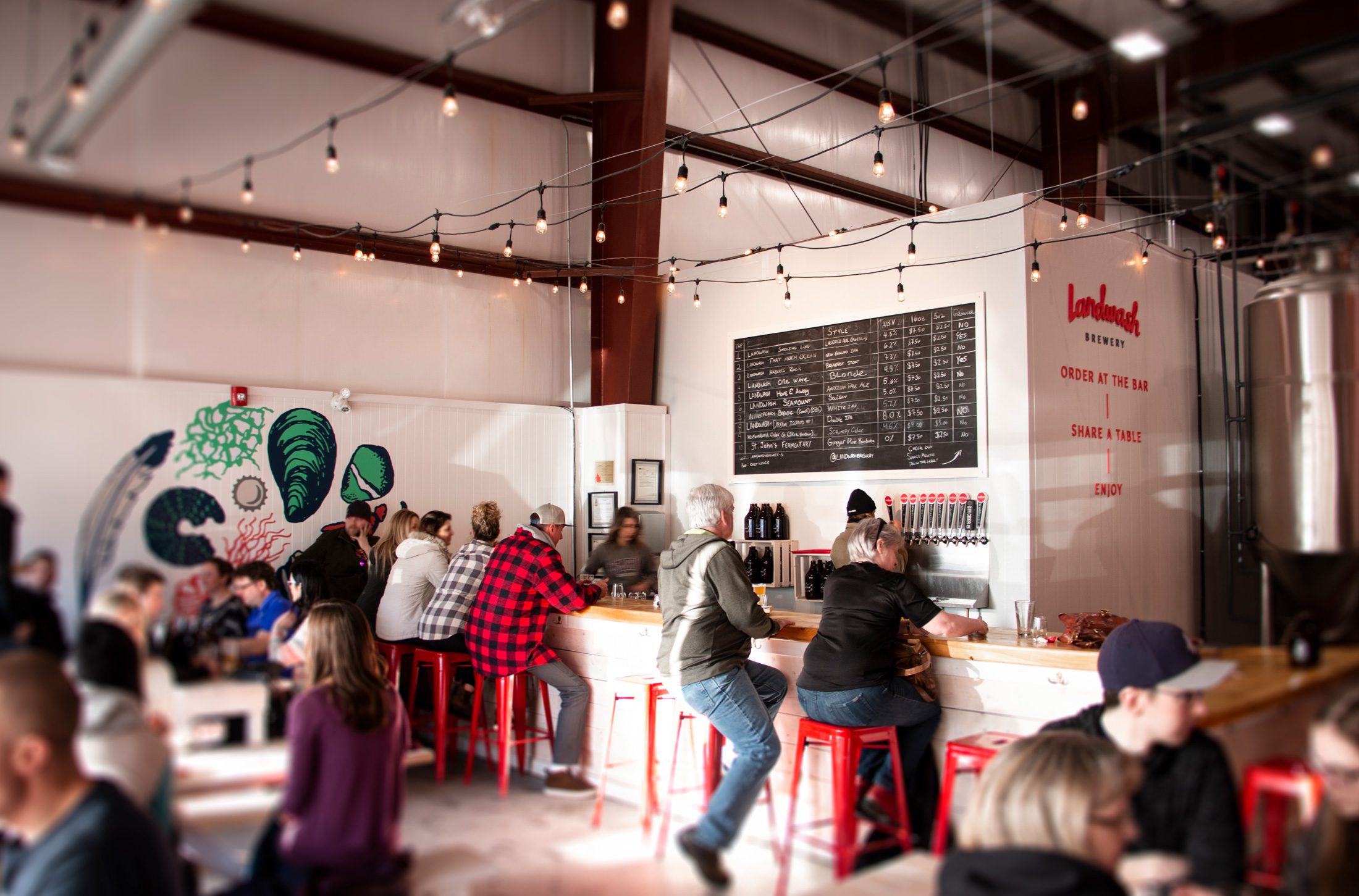 An image of a bustling Landwash taproom with a bar area and large chalkboard