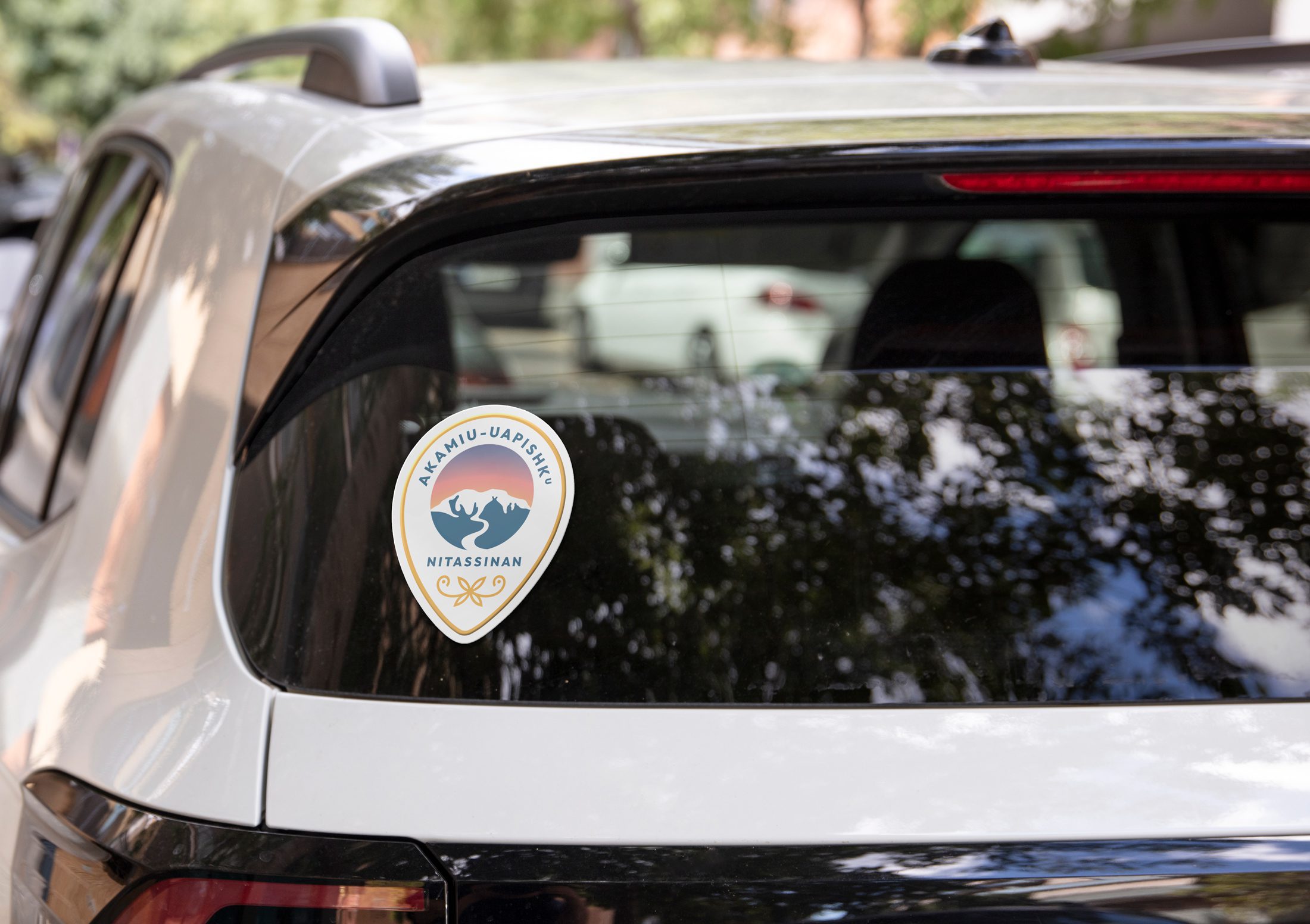 Akamiu-Uapishku branded sticker on the rear window of a white SUV on a sunny day